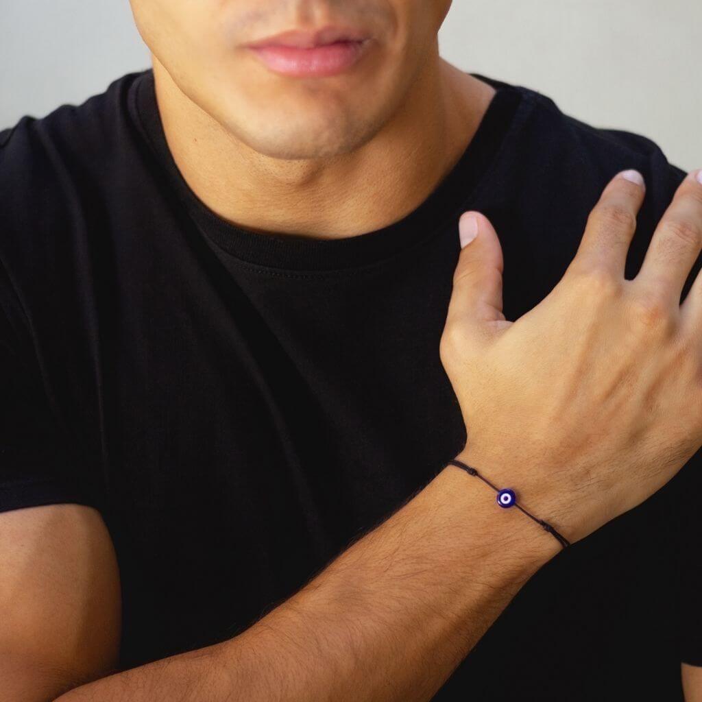 Black string bracelet with an evil eye charm worn by a man, casual and versatile - Luck Strings.