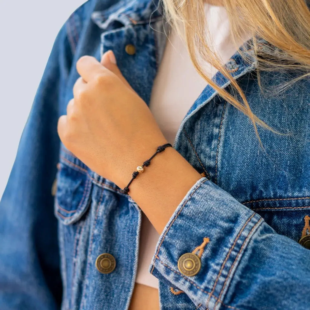 Women showcasing a black string bracelet with 14K yellow gold bead - Luck Strings