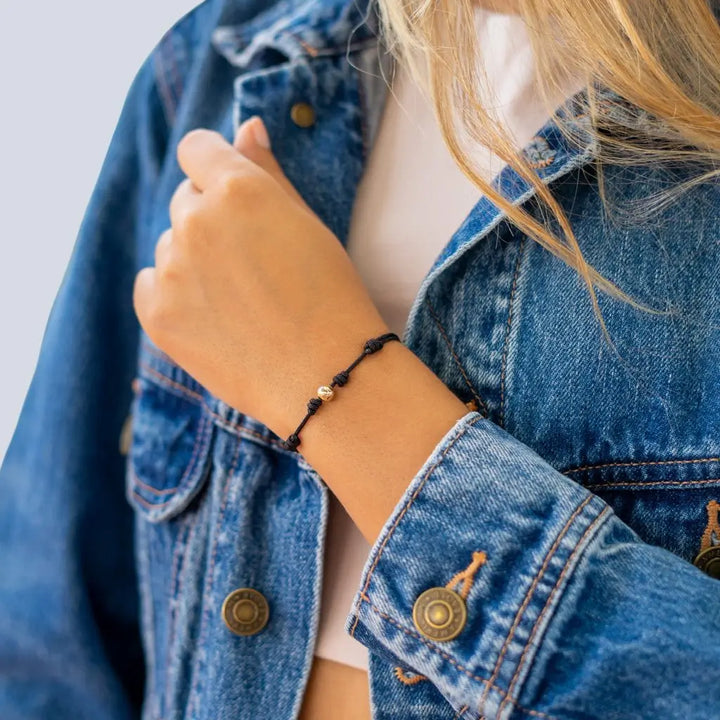 Women showcasing a black string bracelet with 14K yellow gold bead - Luck Strings