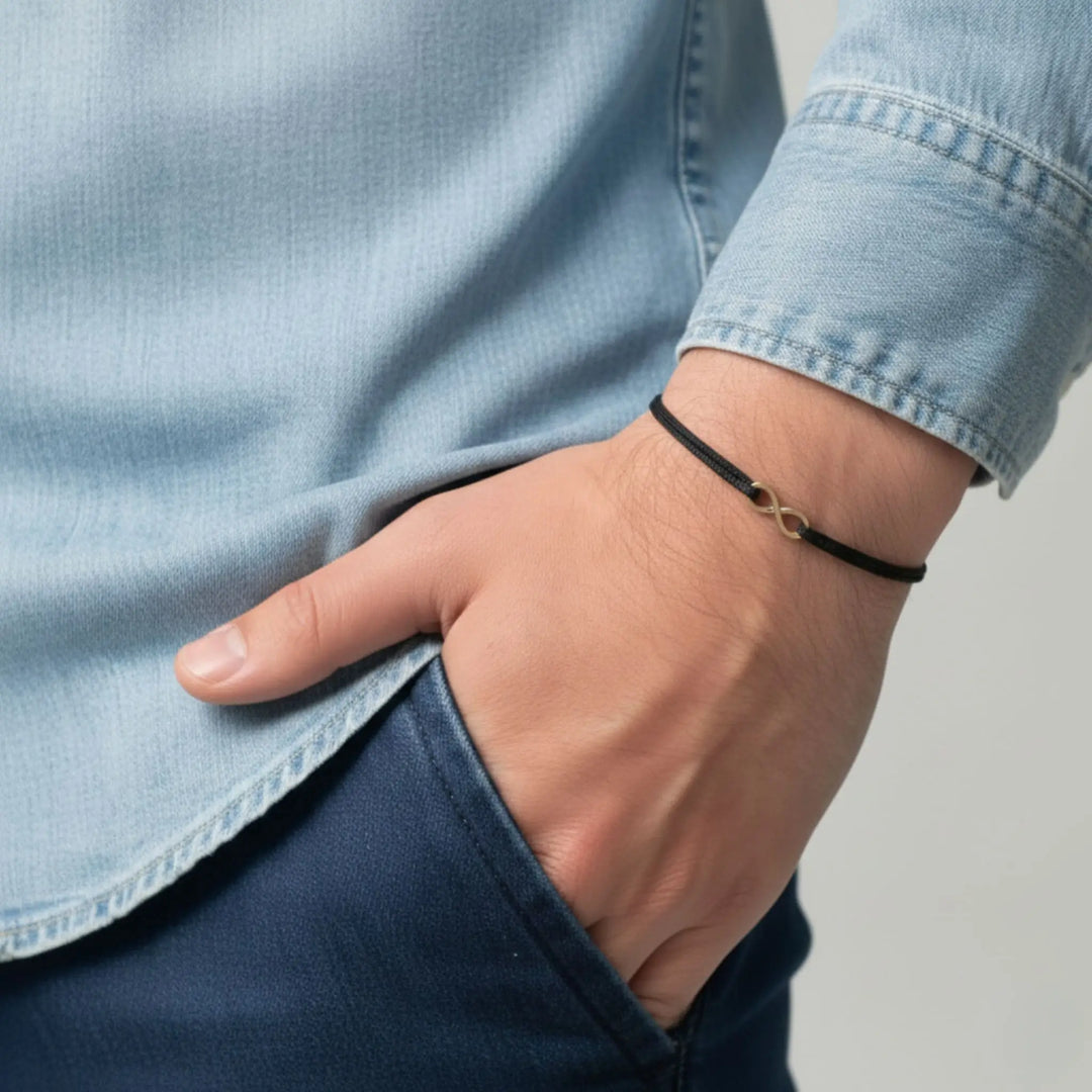Person wearing a black bracelet with a gold infinity on a neutral background