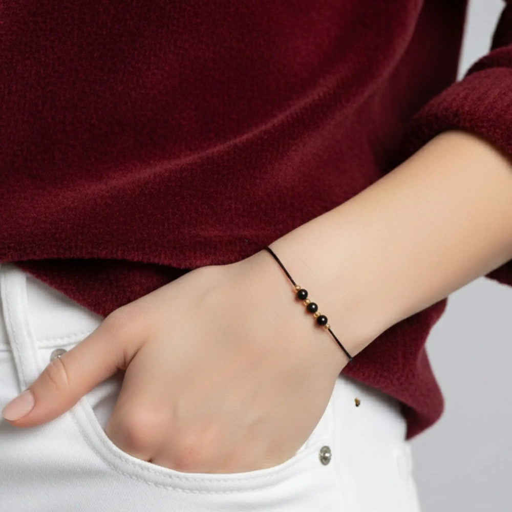 Person wearing a black tourmaline gold bracelet on a plain background
