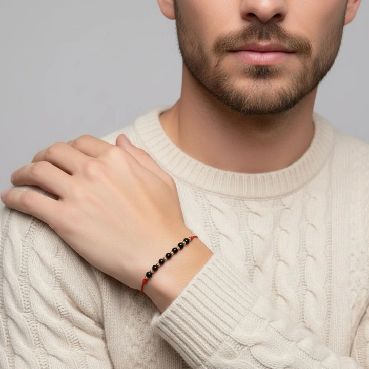 Man wearing a black tourmaline and red cord bracelet on a gray background