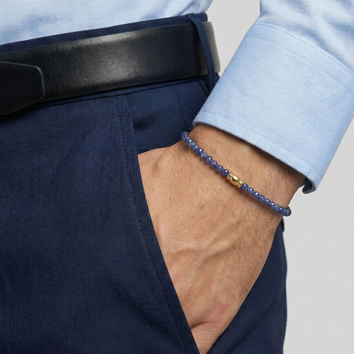 Close-up of a person wearing a blue spphire beaded bracelet on a plain background