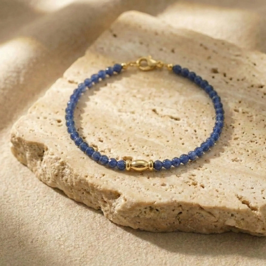 Blue sapphire beaded bracelet with gold clasp on a beige stone surface
