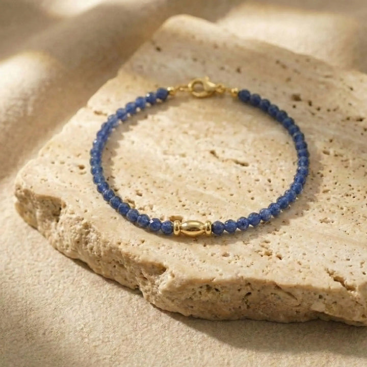 Blue sapphire beaded bracelet with gold clasp on a beige stone surface