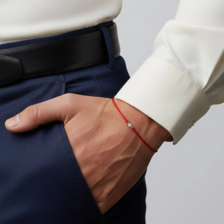 Close-up of a person wearing a  diamond red string bracelet on a plain background