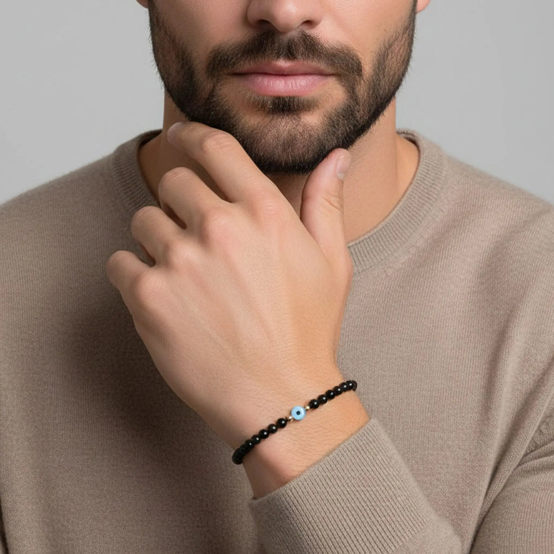 Man wearing a evil eye black tourmaline beaded bracelet with a blue bead on a neutral background