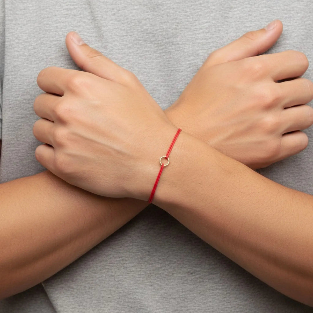 Red string bracelet on a wrist with a gray background
