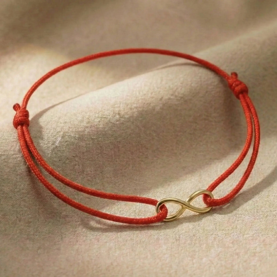 Red cord bracelet with a gold infinity charm on a beige background