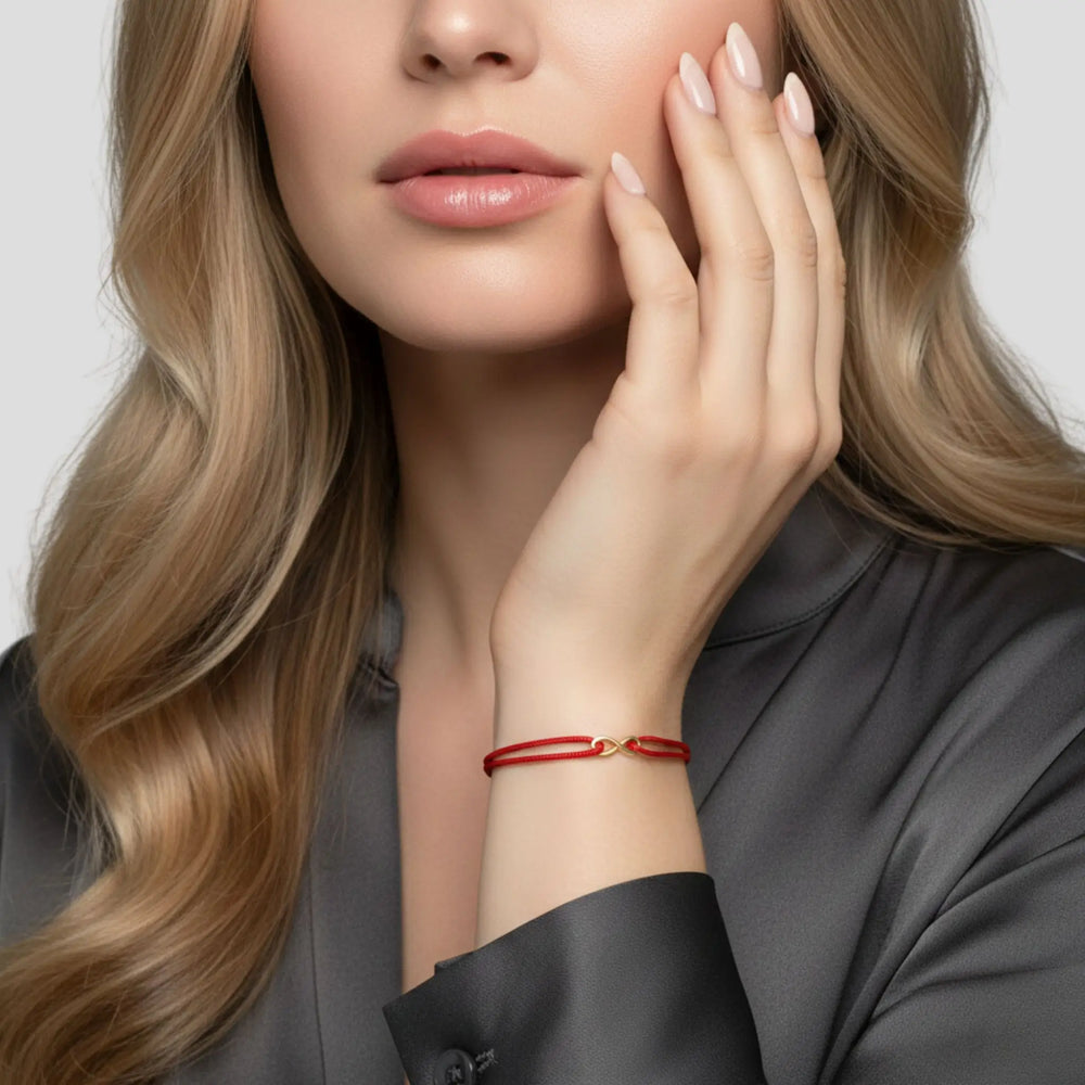Woman wearing a red bracelet with a gold infinity on a neutral background