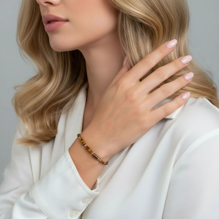 Woman wearing a gold tiger eye bracelet on a plain background