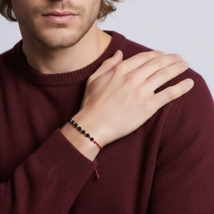 Man wearing a burgundy sweater with a close-up of his hand and bracelets.