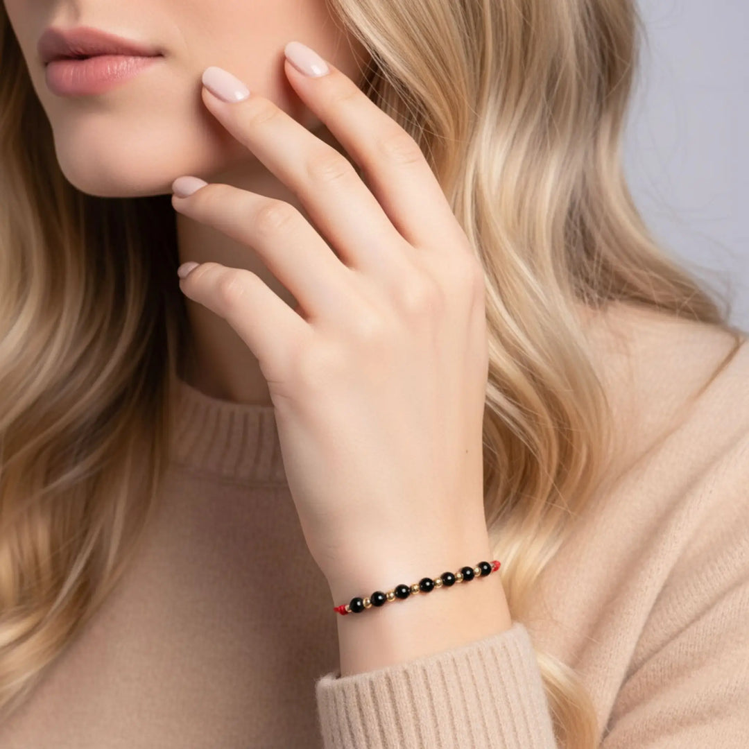Close-up of a woman's hand wearing a red and black tourmaline solid gold beaded bracelet on a neutral background