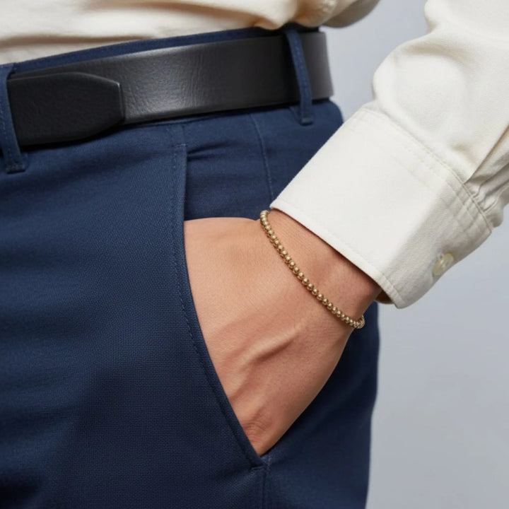 Person wearing navy pants with a white shirt and gold bracelet on a neutral background