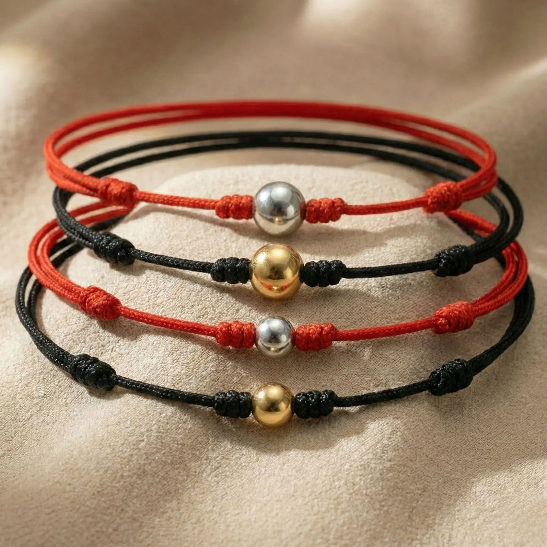 Four bracelets with red and black cords and gold and silver beads on a beige surface