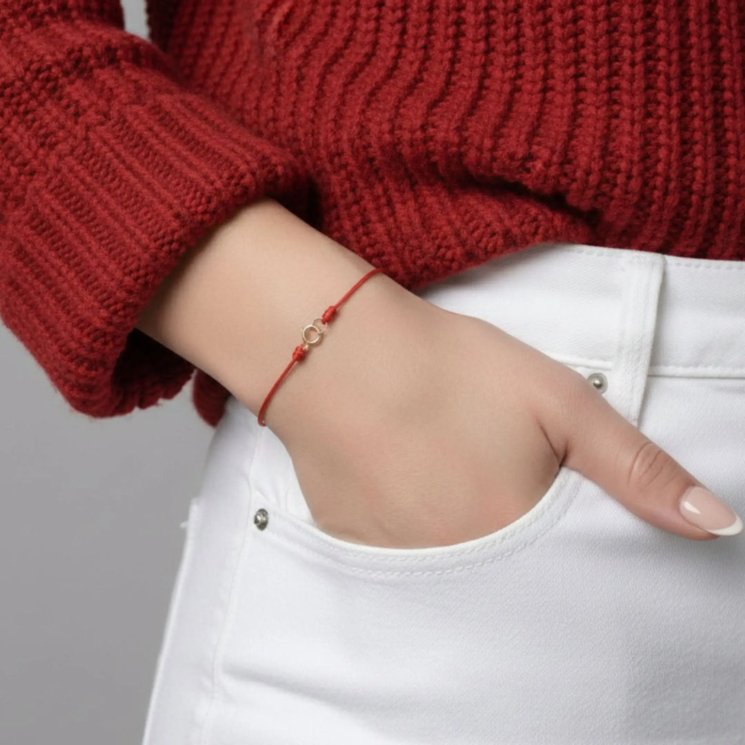 Hand wearing a red bracelet with a plain background