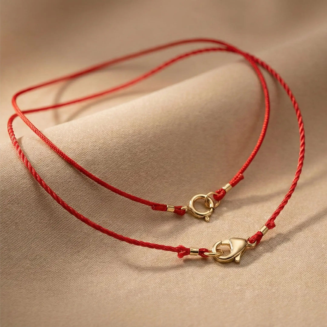 Red string bracelet with gold clasp on a beige fabric background