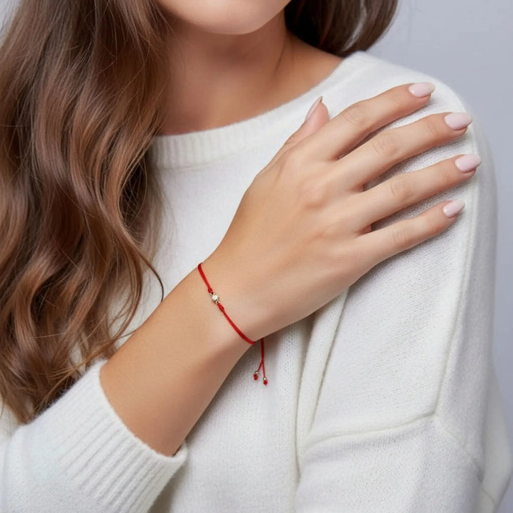 Woman wearing a gold diamond red bracelet on her wrist, with a plain background