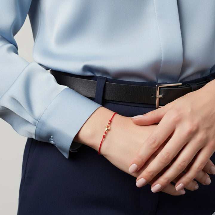 Person wearing a light blue shirt and dark pants with a solid gold red bracelet on a neutral background