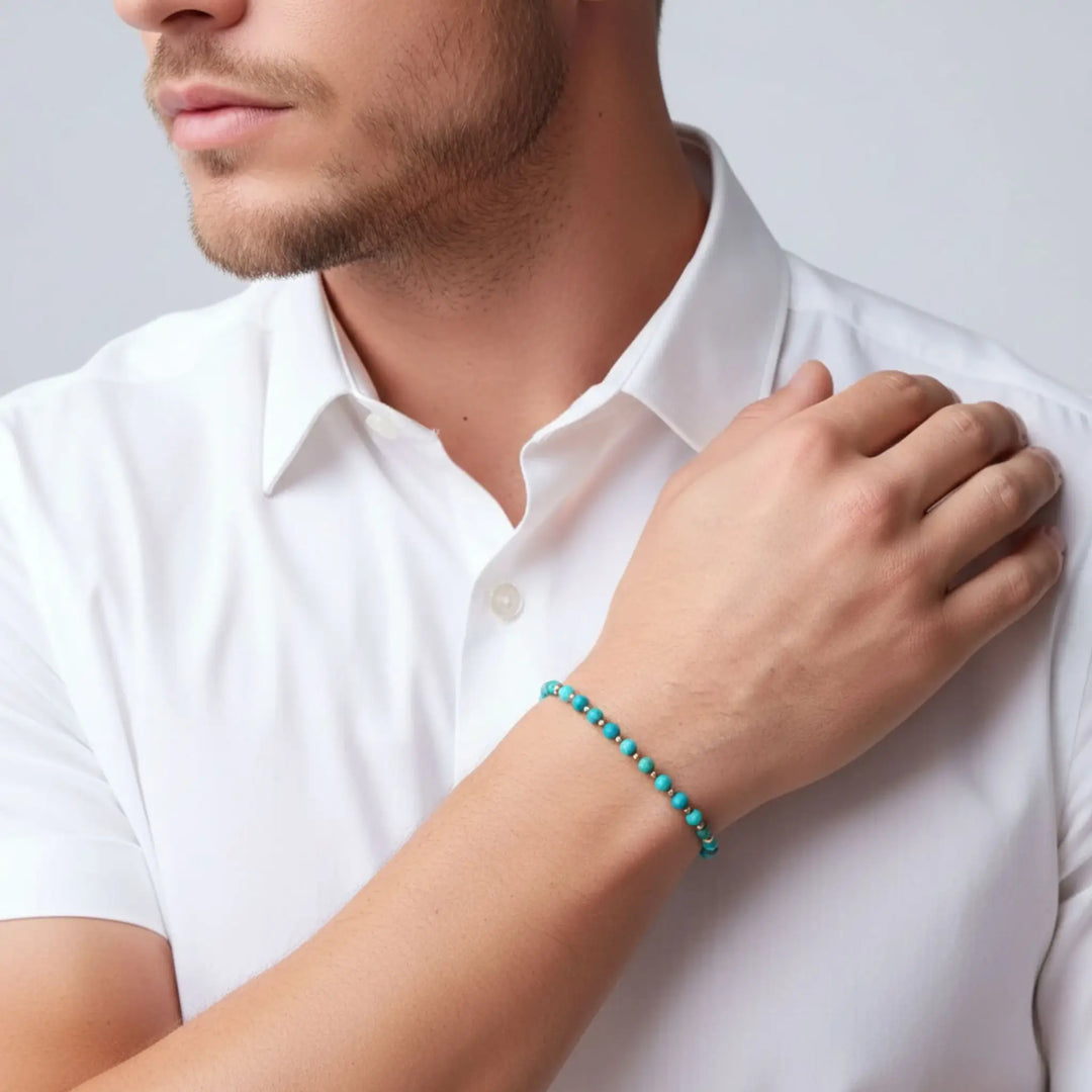 Man wearing a turquoise beaded bracelet on a plain background