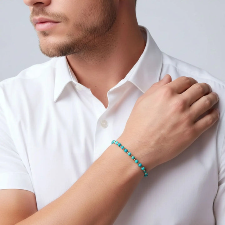 Man wearing a turquoise beaded bracelet on a plain background
