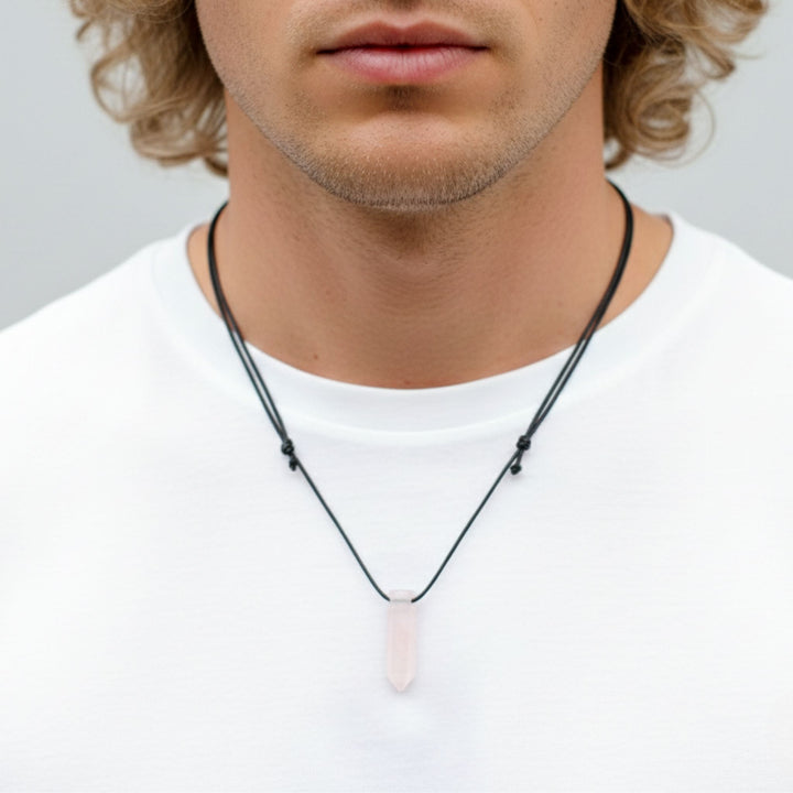 Man wearing a necklace with a pink crystal pendant on a plain background