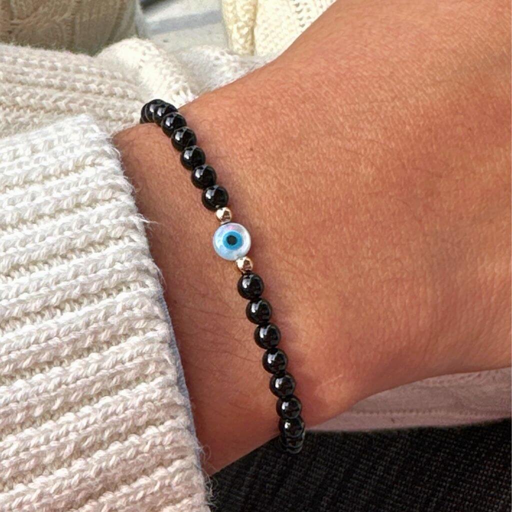 14K Gold and Black Tourmaline bracelet with Mother of Pearl evil eye on a wrist, highlighting the gold accents and snug fit - Luck Strings