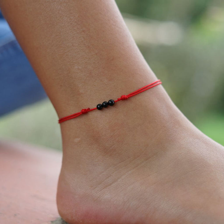 Adjustable tourmaline red string anklet with 4mm beads, modeled on a woman's ankle, symbolizing protection and good luck - Luck Strings