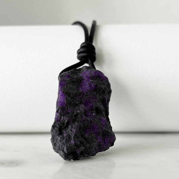 A one-of-a-kind Raw Sugilite Gemstone Pendant showcasing its distinctive deep purple color, suspended from a sleek cord, symbolizing spiritual growth and emotional healing - Luck Strings.