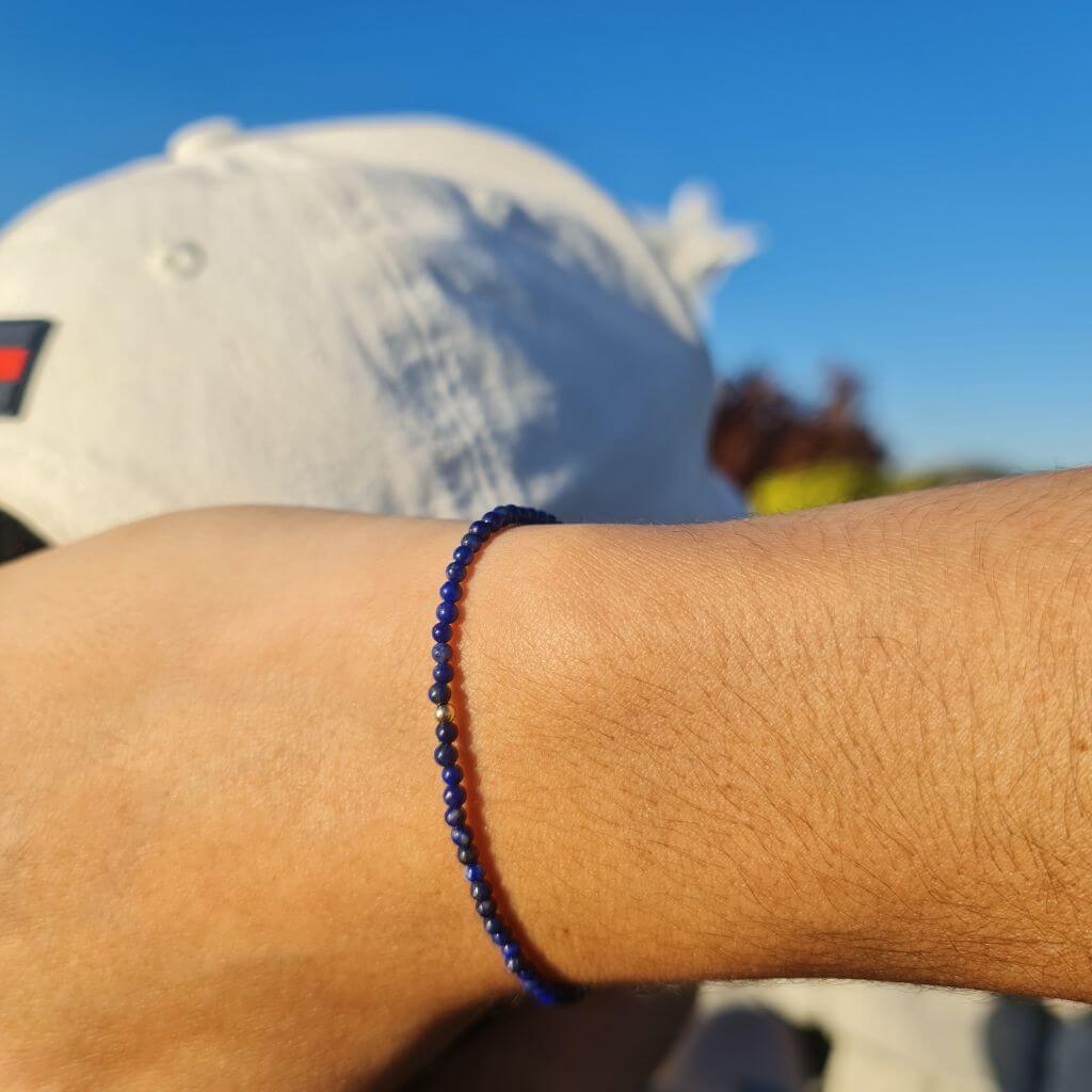 Man showcasing a Lapis Lazuli & 14K Solid Gold Minimalist Bracelet on his wrist, highlighting the rich blue lapis against the luxurious gold - Luck Strings.