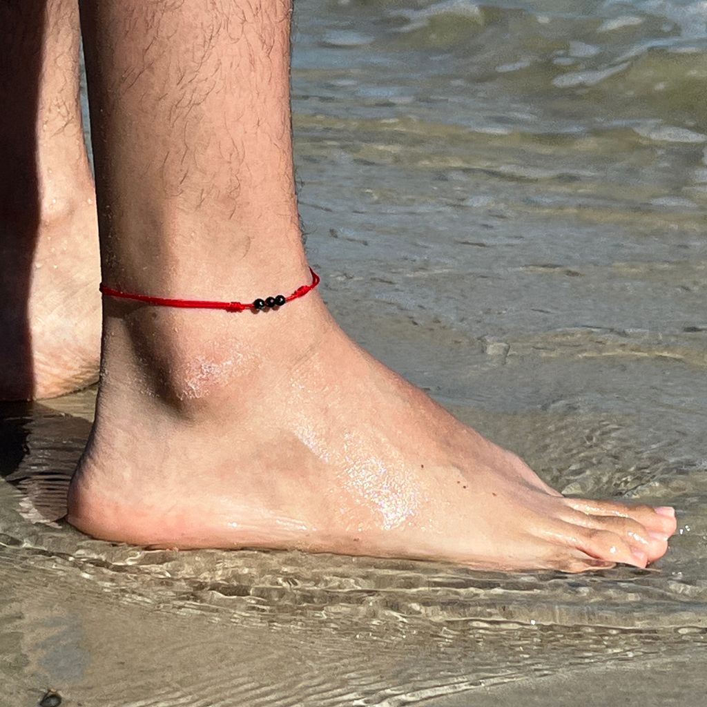 Adjustable tourmaline red string anklet with 4mm beads, modeled on a woman's ankle, symbolizing protection and good luck - Luck Strings
