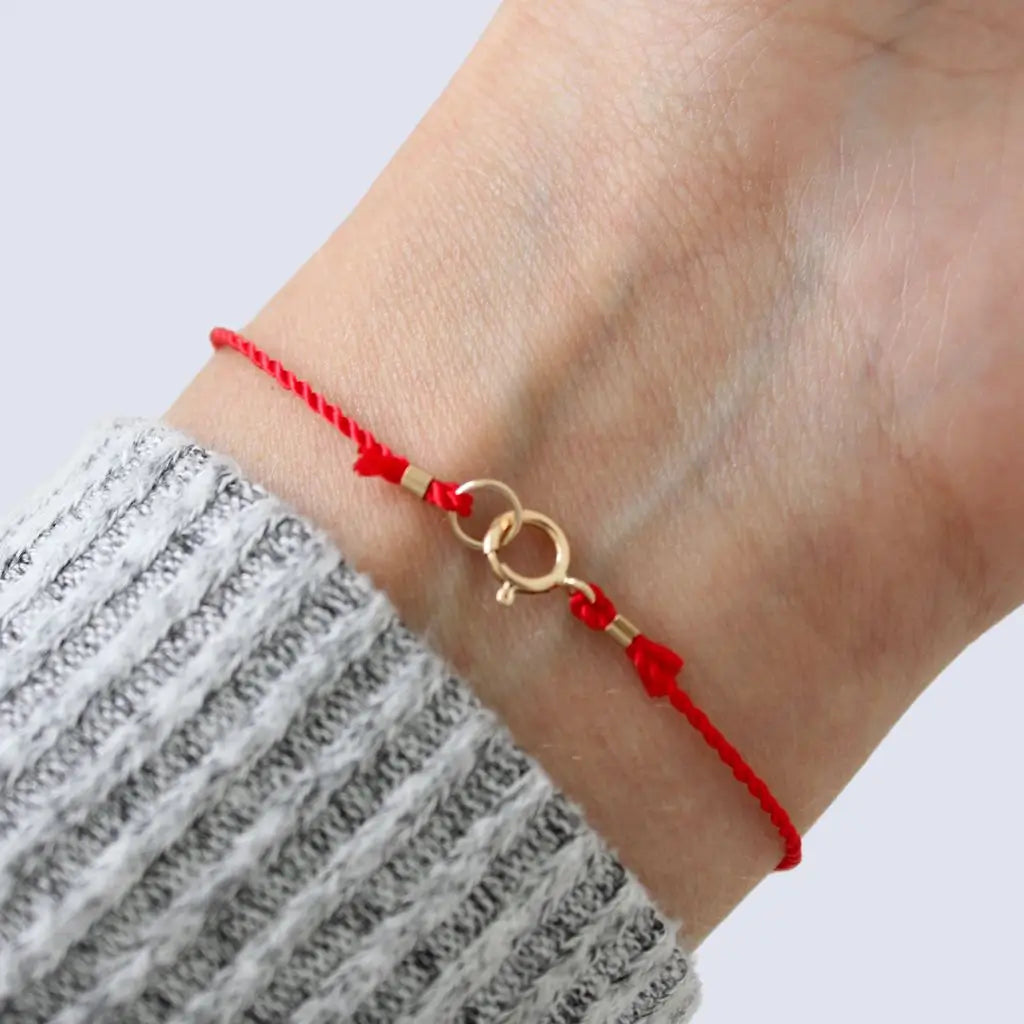 Luck Strings red string bracelet with 14k solid yellow gold triple beads on a person's wrist.
