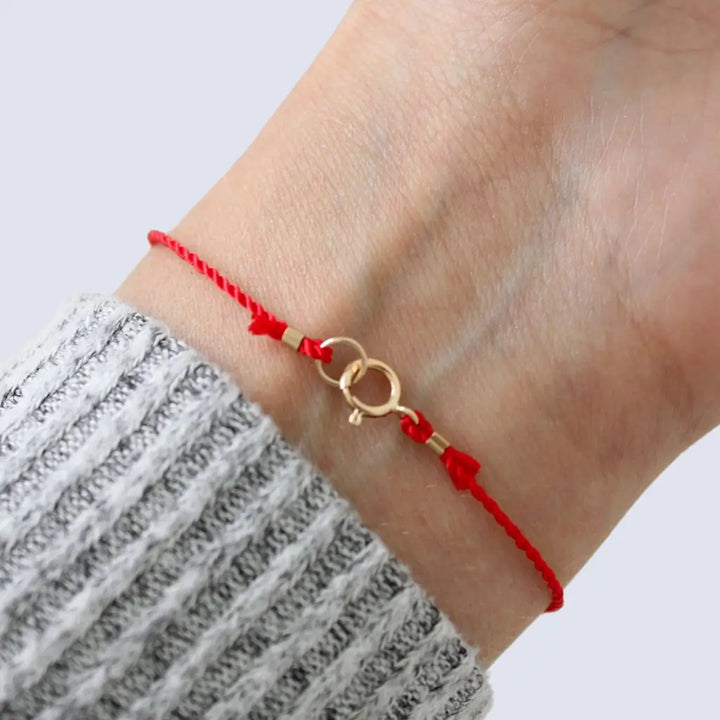 Luck Strings red string bracelet with 14k solid yellow gold triple beads on a person's wrist.