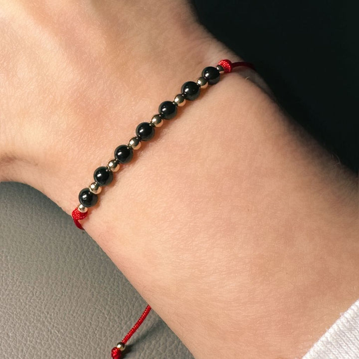 Woman wrist with a Black Tourmaline & 14K Gold Red Bracelet, elegantly combining the powerful energy of black tourmaline with the sophistication of 14K gold - Luck Strings.