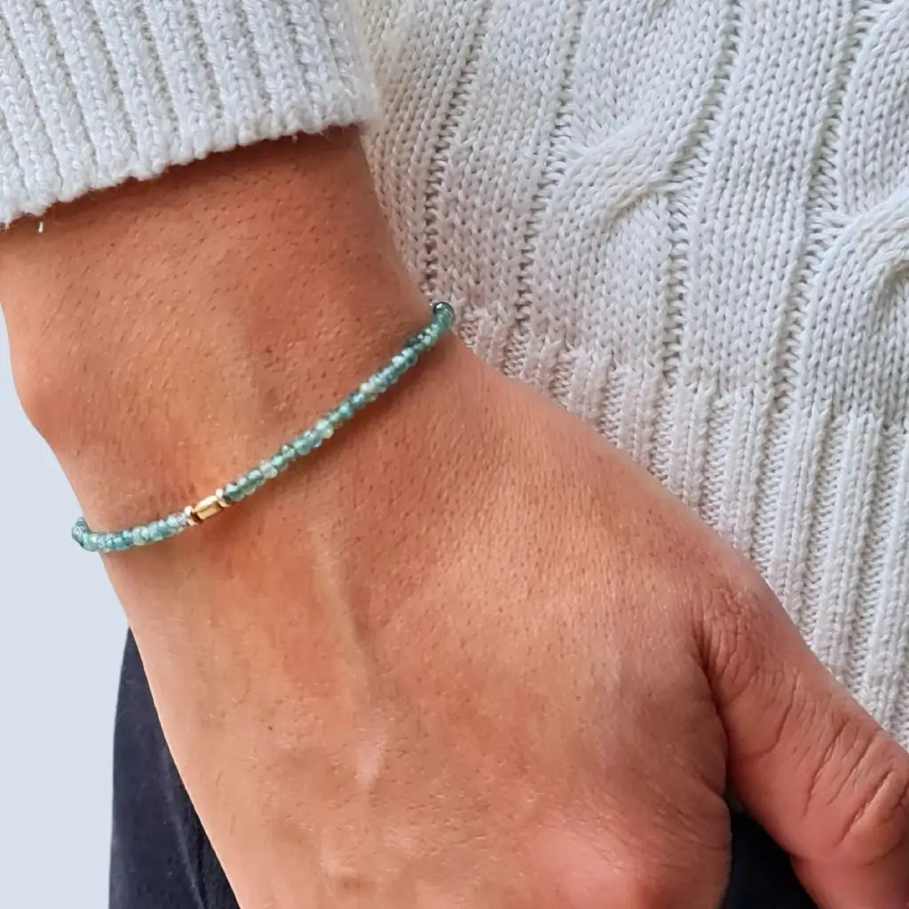 A person's wrist wearing a blue tourmaline bracelet with 14K gold accents.