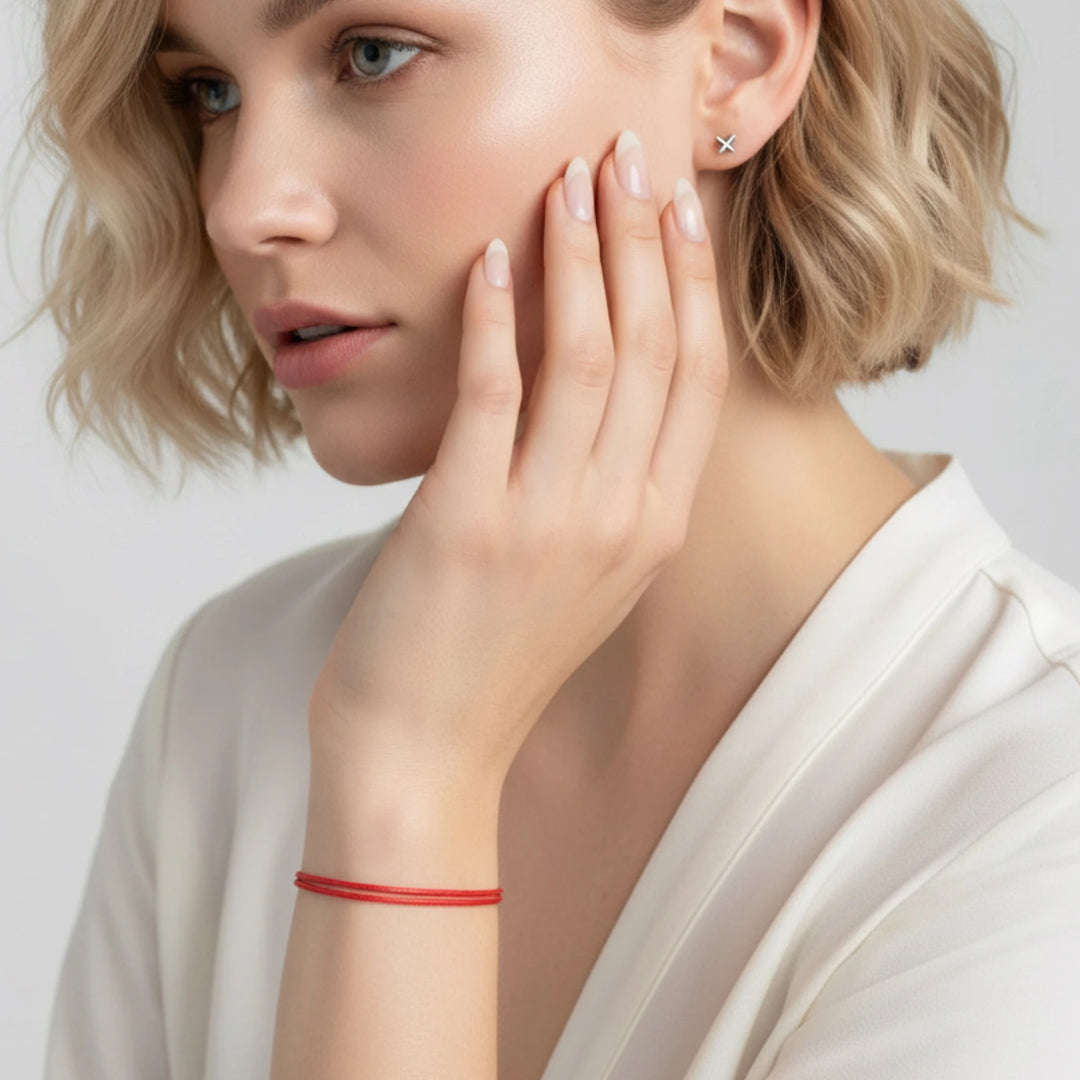 Woman wearing a red bracelet and gold earring on a plain background