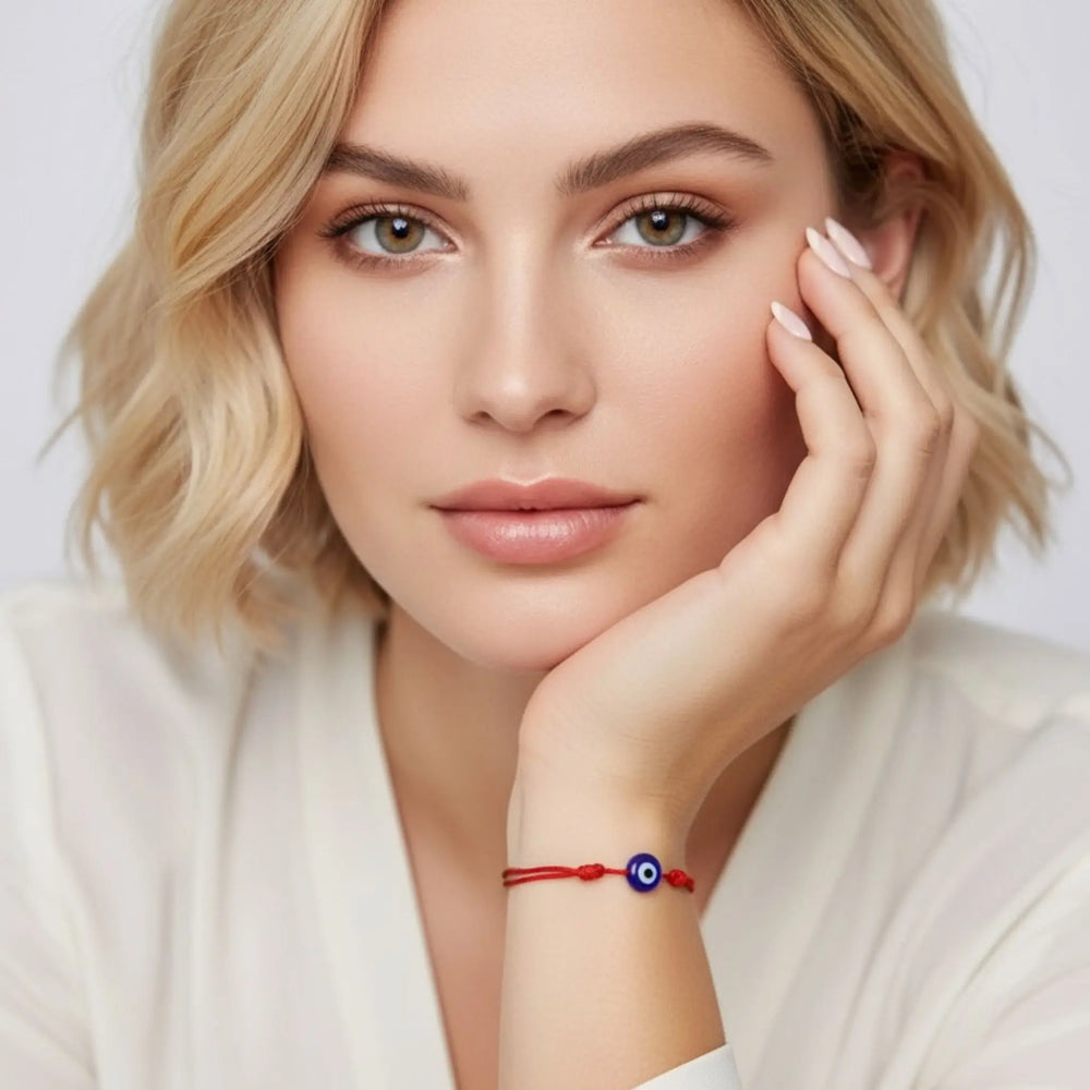 Woman wearing a red bracelet with a blue eye design on a plain background