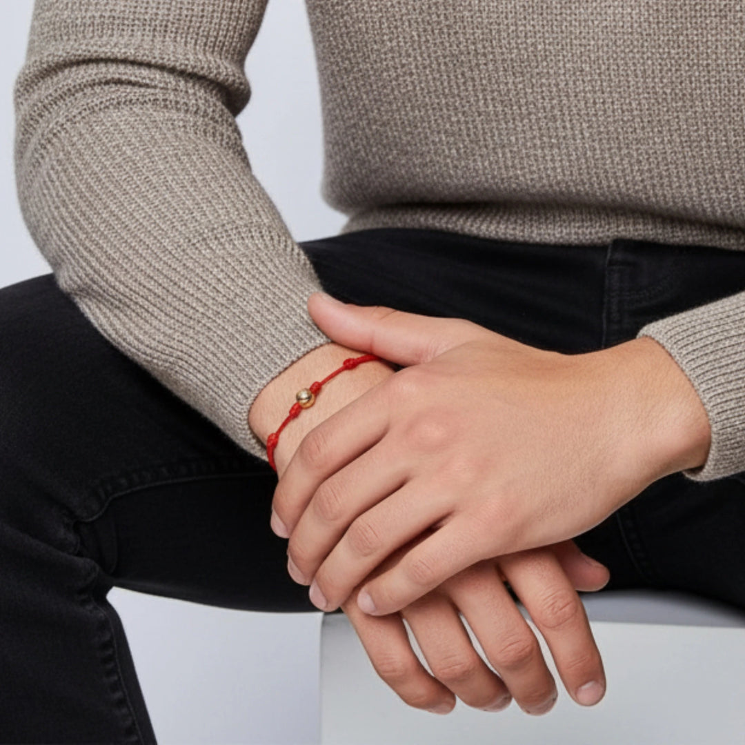 Person wearing a red solid gold bead bracelet on a plain background