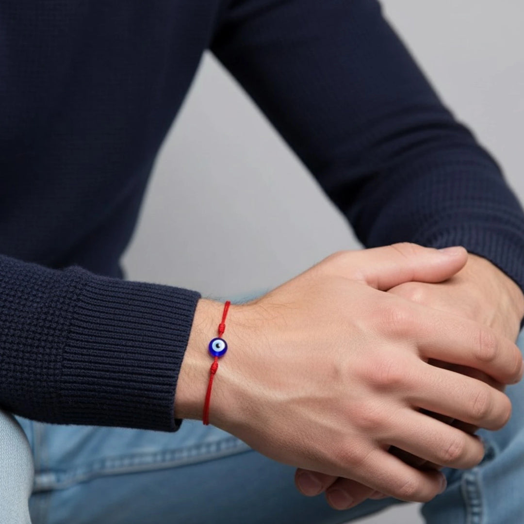 Person wearing a red bracelet with a blue bead on a neutral background