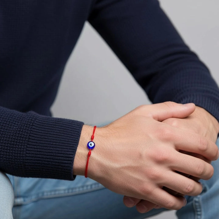 Person wearing a red bracelet with a blue bead on a neutral background