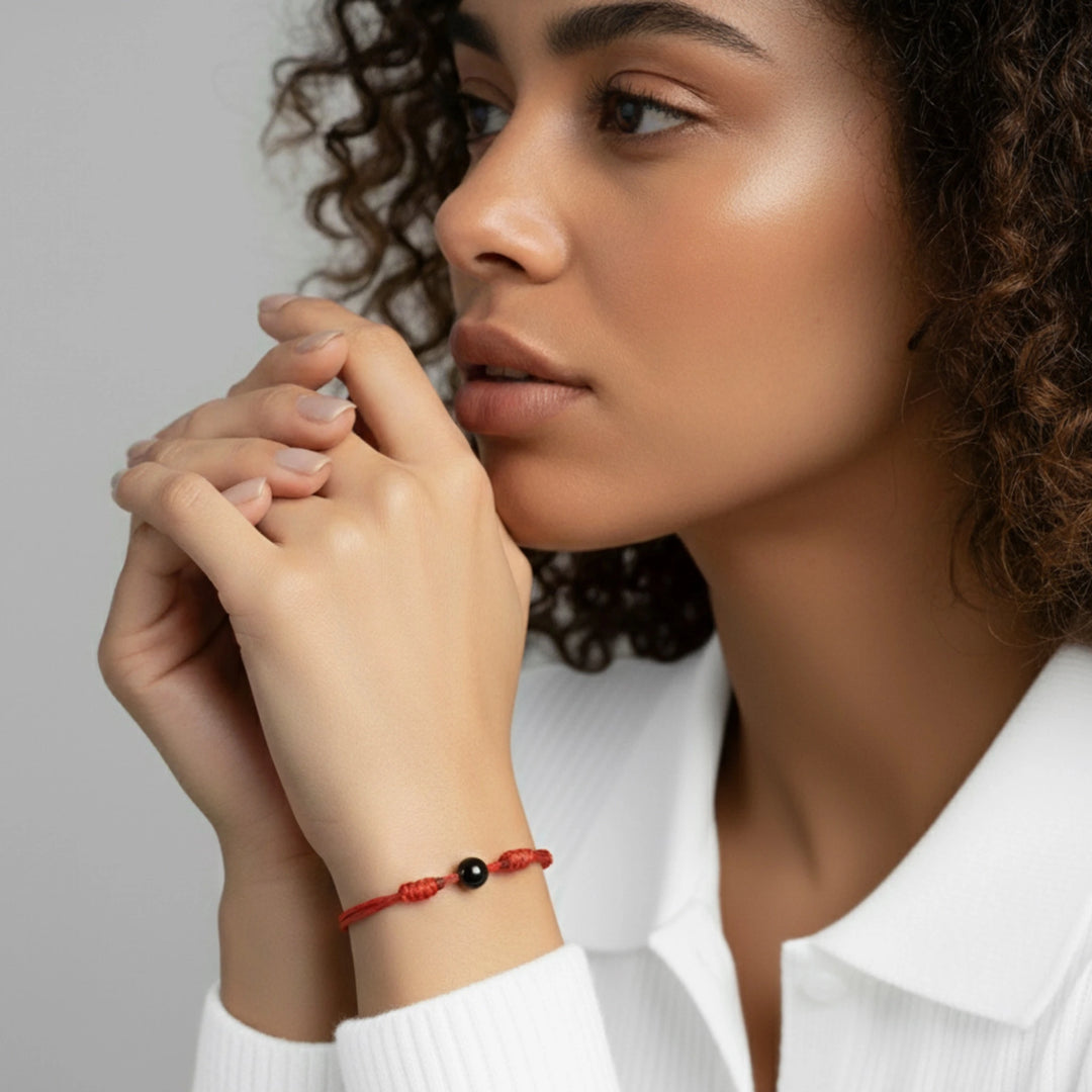 Woman wearing a red bracelet with a black tourmaline bead on a neutral background