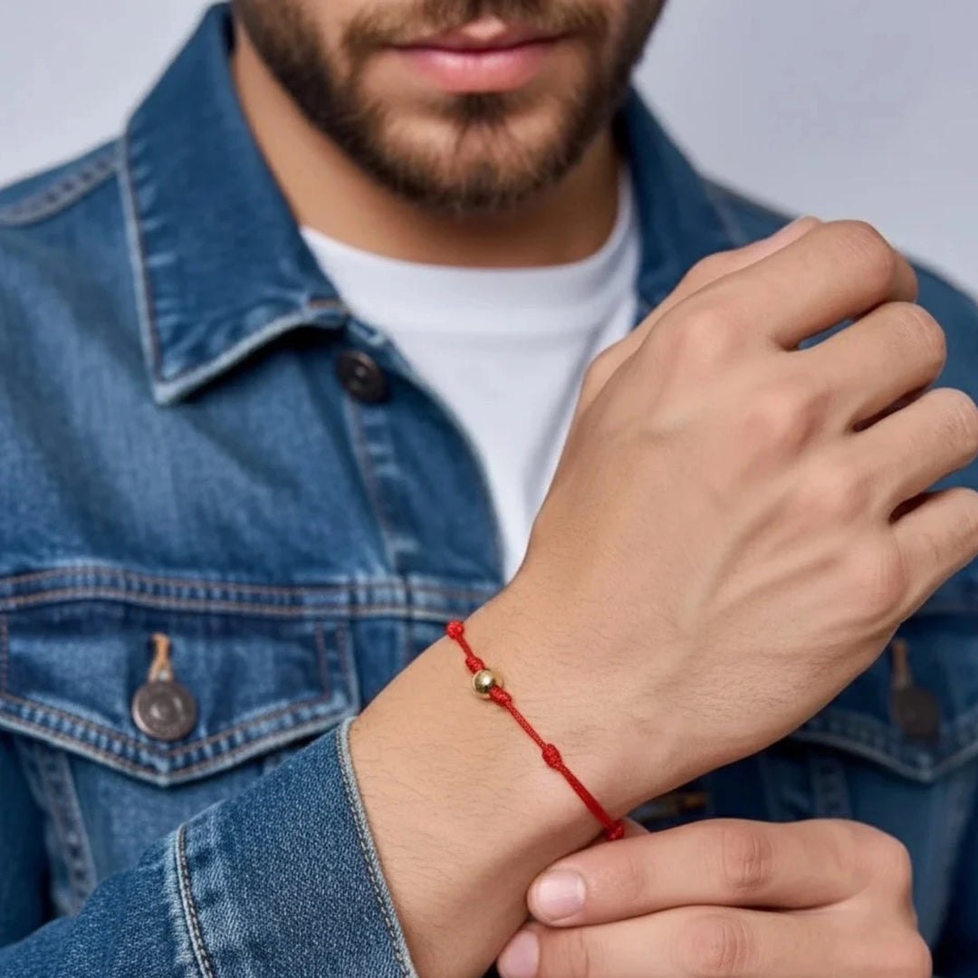 Man wearing a red solid gold bead bracelet on his wrist with a denim jacket.
