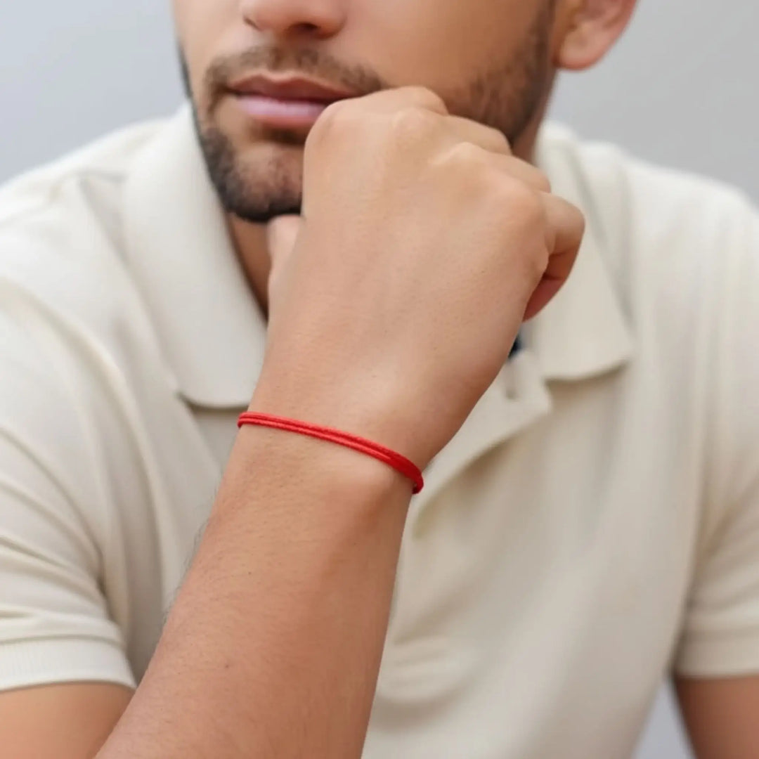 Person wearing a red bracelet on their wrist with a neutral background