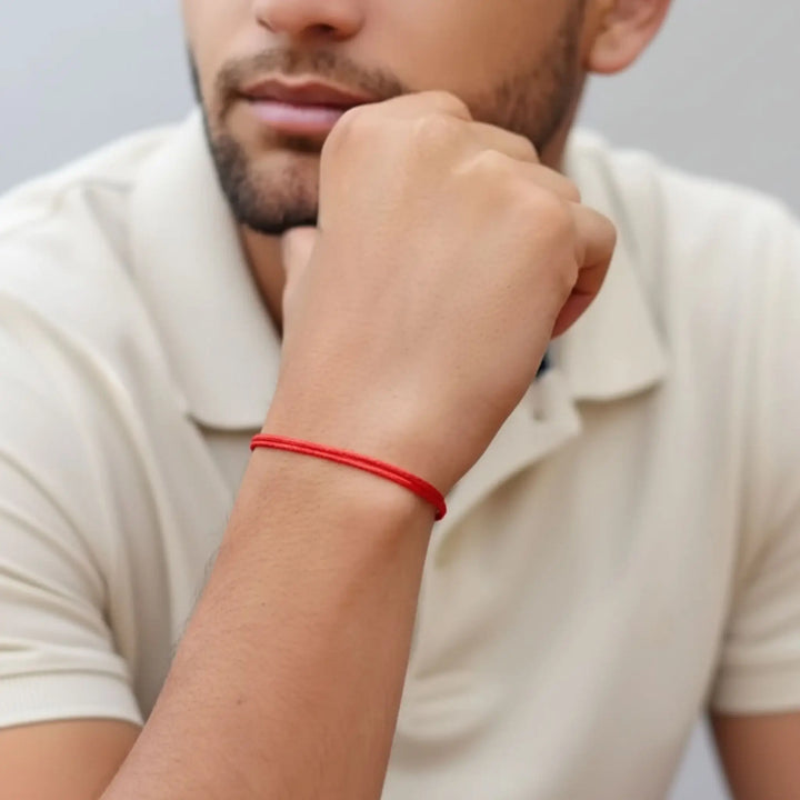 Person wearing a red bracelet on their wrist with a neutral background
