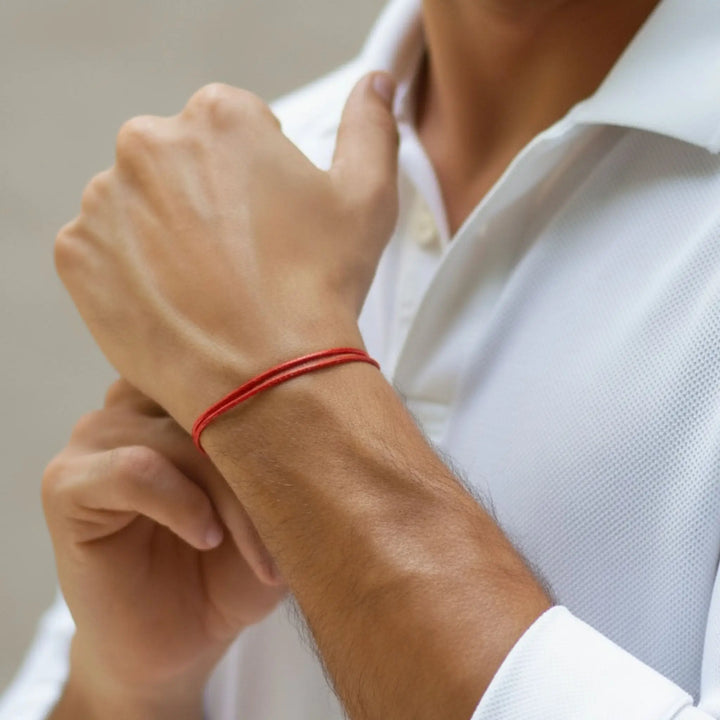 Person wearing a red bracelet on a neutral background