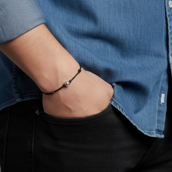 Person wearing a black solid gold beaded bracelet on a wrist with a blue shirt and black pants.