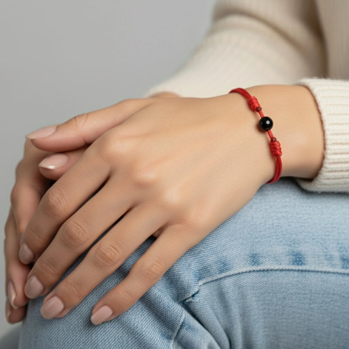 Hand wearing a red bracelet with a black tourmaline bead, sitting on a light blue surface.