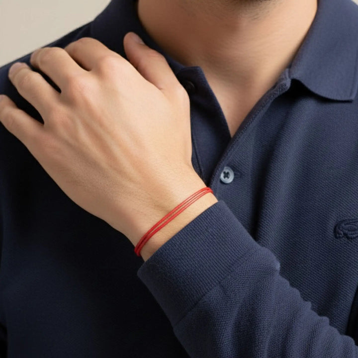 Person wearing a navy blue polo shirt with a red bracelet on a neutral background