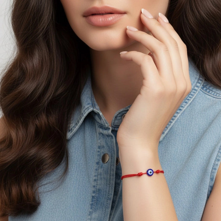 Woman wearing a red bracelet with a blue bead on her wrist, wearing a denim jacket.