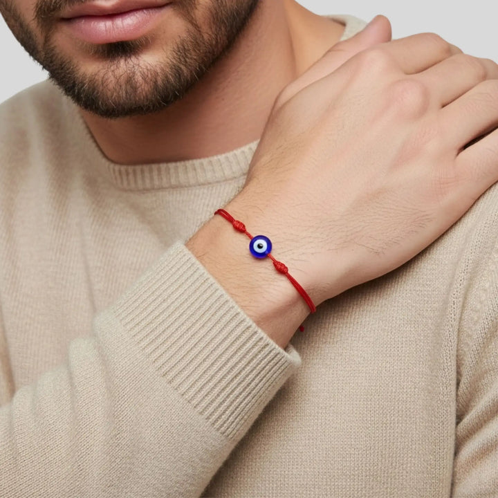Person wearing a red bracelet with an eye charm on a neutral background